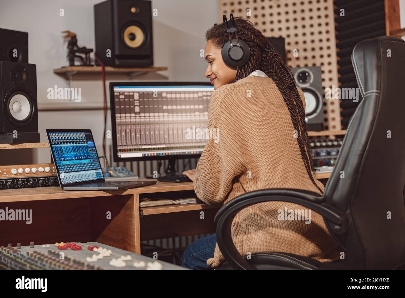 Afrikanische nette Bloggerin nimmt Online-Podcast mit Laptop, Kopfhörer und Mikrofon in professionellen Musikstudio Stockfoto