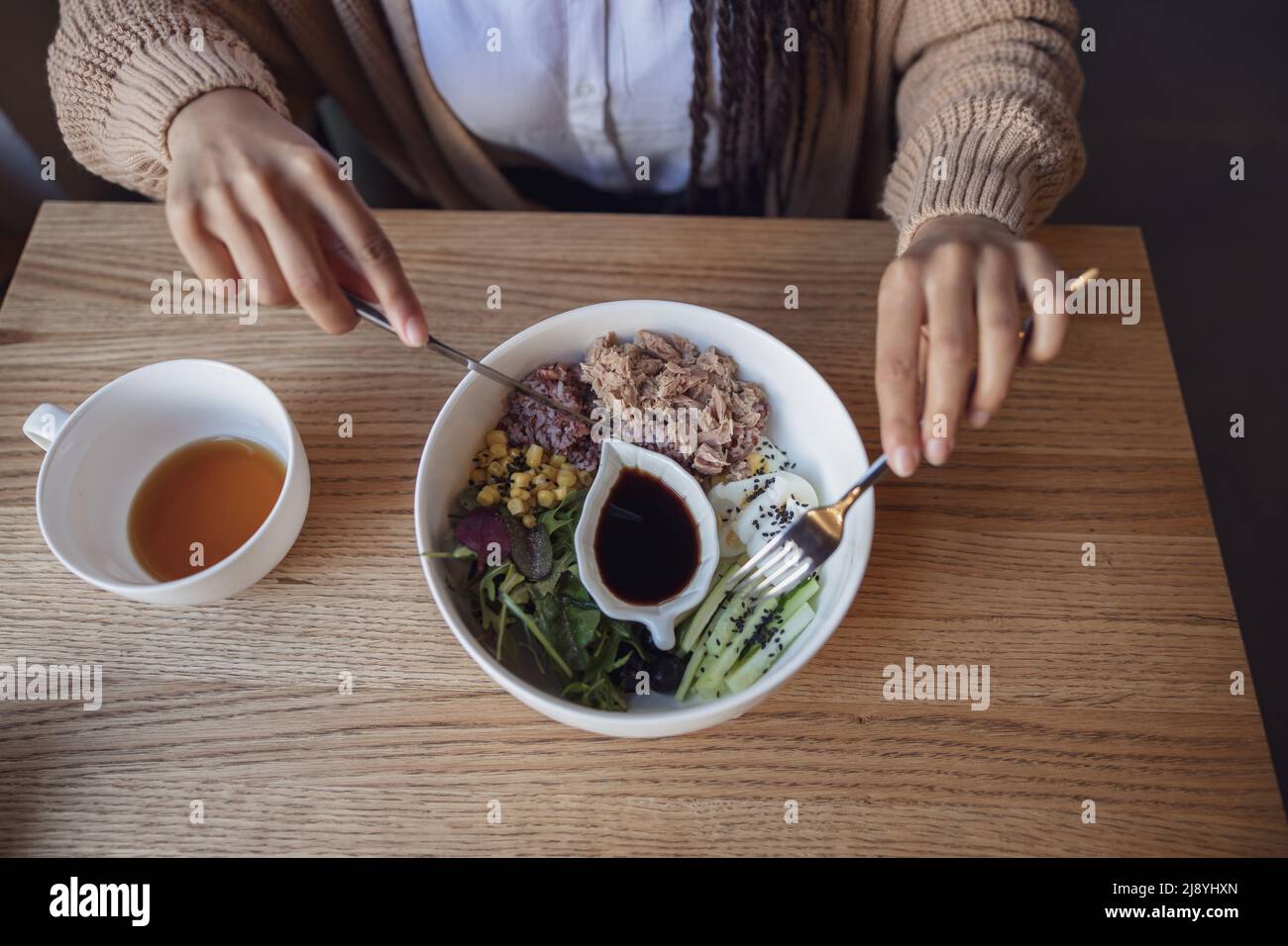 Draufsicht auf weibliche Hände, die Gabel und Messer halten und köstliche gesunde Lebensmittel in einer weißen Keramikschale essen Stockfoto