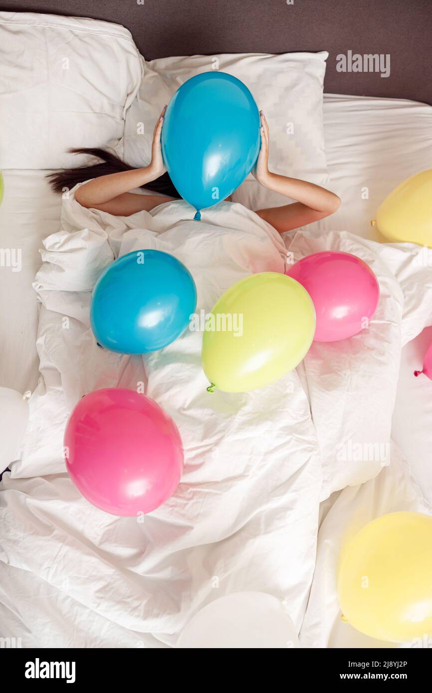 Junge Frau liegt im Bett mit bunten Ballons zu Hause Stockfoto