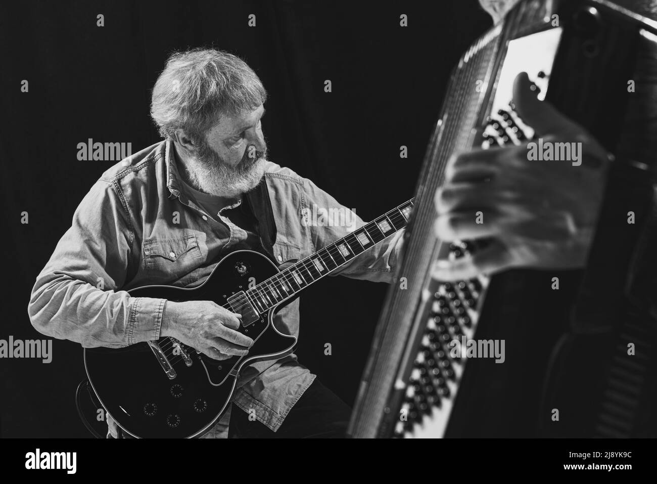 Schwarz-Weiß-Porträt von zwei älteren Männern, Musikern mit Gitarre und Akkordeon im Musikstudio. Konzept von Kunst, Musik, Stil und Kreation. Monochrom Stockfoto