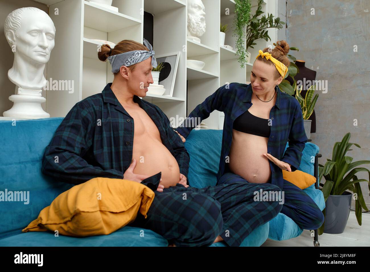 Eine Schwangeren und ihr Mann machen lustige Schwangerschaftsfotos. Der Mann zeigt seinen Bauch vor der Schwangeren Stockfoto