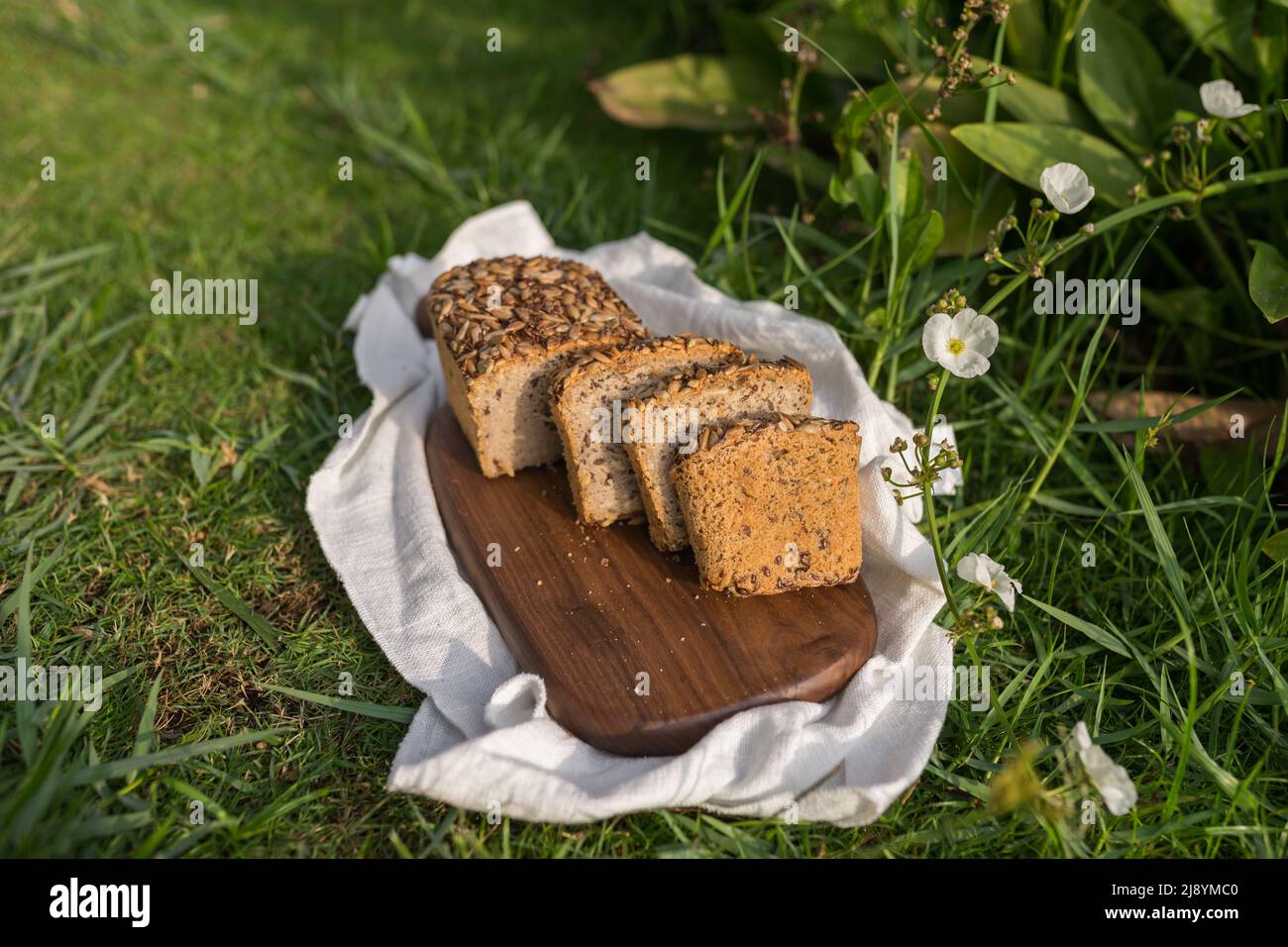 Hausgemachtes graues Brot mit Samen auf dem Holzbrett mit der weißen Stoffserviette auf dem grünen Gras. Hochwertige Fotos Stockfoto