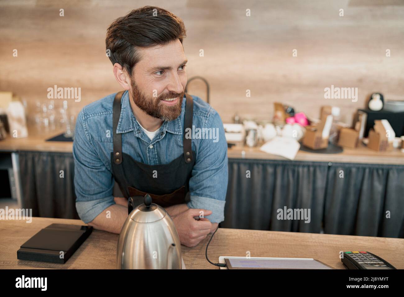 Lächelnder Barista, der mit dem Kunden spricht, während er hinter einem Tresen steht Stockfoto