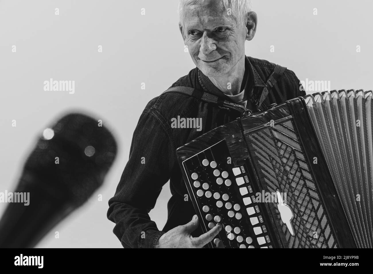 Monochromes Porträt eines senioten Mannes, Retro-Musiker, der die Ziehharmonika auf weißem Hintergrund spielt. Konzept von Kunst, Musik, Stil, ältere Generation Stockfoto