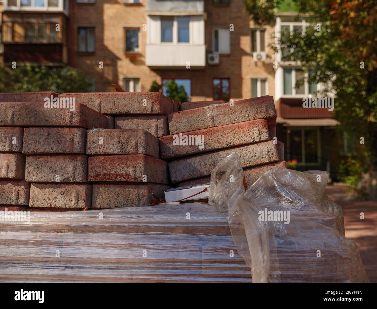 Ein Stapel Pflasterfliesen und Zigarettenpackungen im Vordergrund und ein altes rotes Ziegelgebäude, das von der untergehenden Sonne im Hintergrund in Kiew, Ukraine, beleuchtet wird. Stockfoto