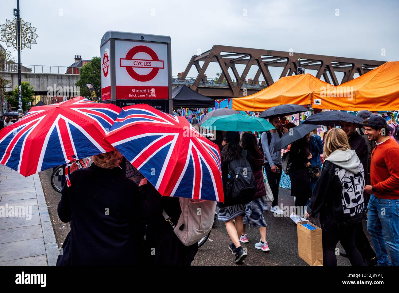 Brick Lane Sunday Market in Londons East End Shoreditch Gegend an einem regnerischen Tag. Shopper und Touristen laufen die Brick Lane entlang mit Union Jack Schirmen. Stockfoto