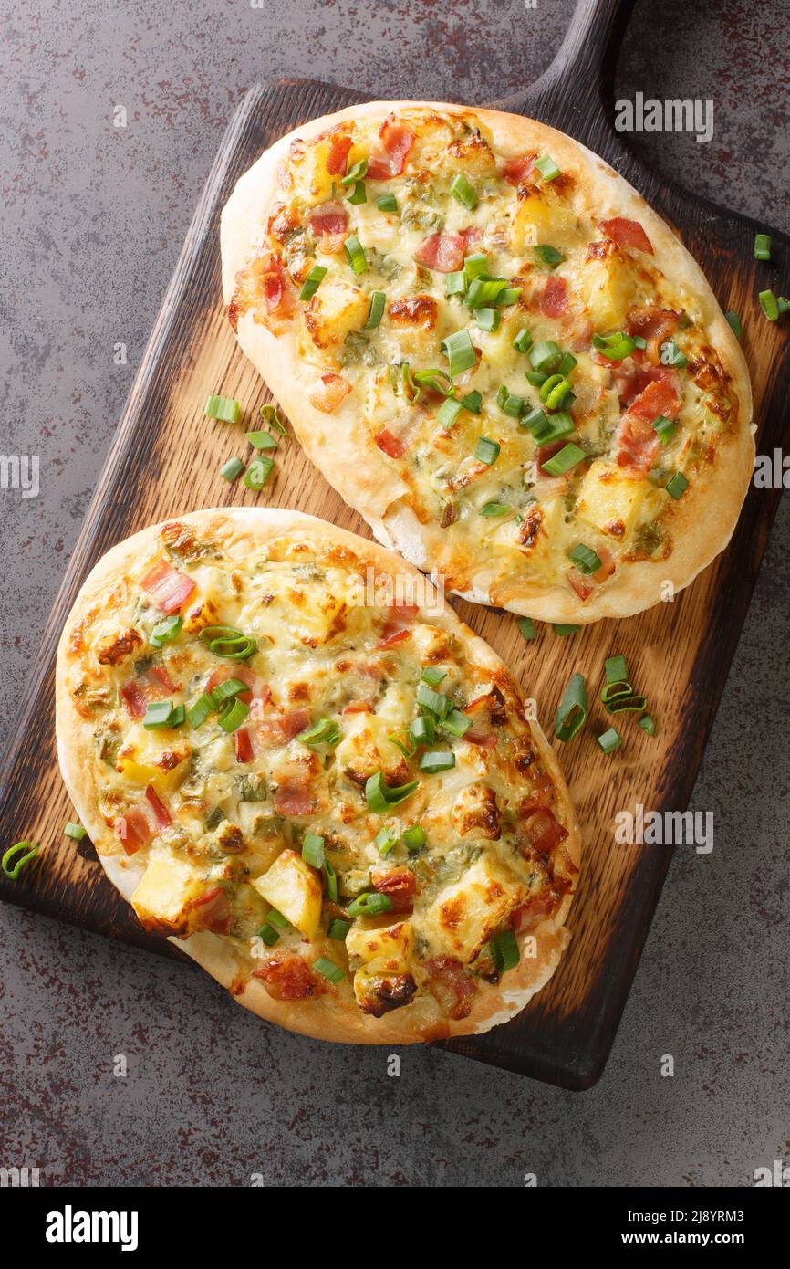 Deutsche Pizza Schwäbische Dinnete mit Kartoffeln, Zwiebeln und Speck aus nächster Nähe auf einem Holzbrett auf dem Tisch. Vertikale Draufsicht von oben Stockfoto