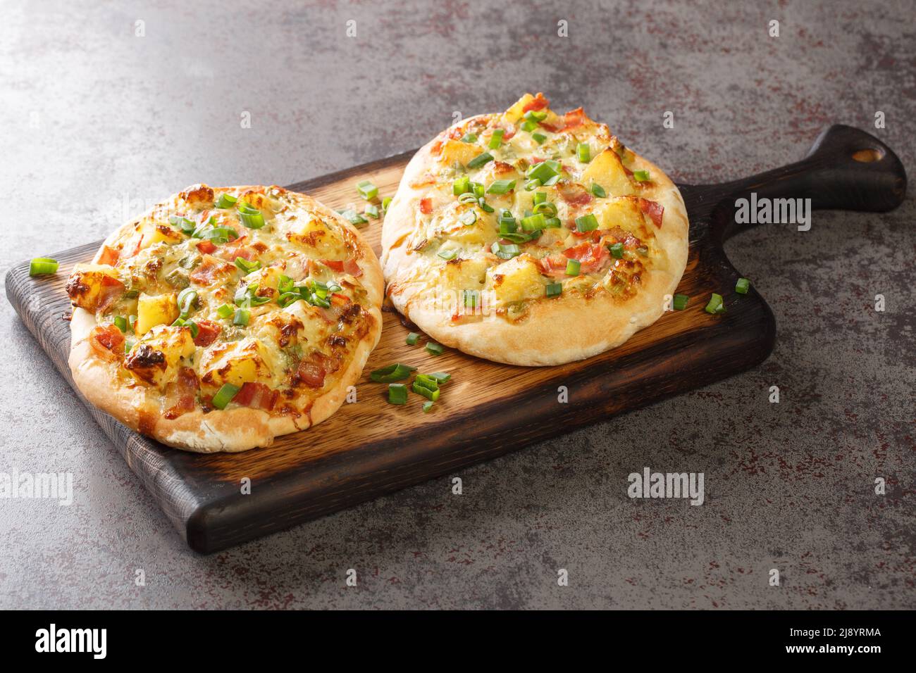 Deutsche Pizza-tart Flambee Schwäbische Dinnete mit Kartoffeln, Zwiebeln und Speck aus der Nähe auf einem Holzbrett auf dem Tisch. Horizontal Stockfoto