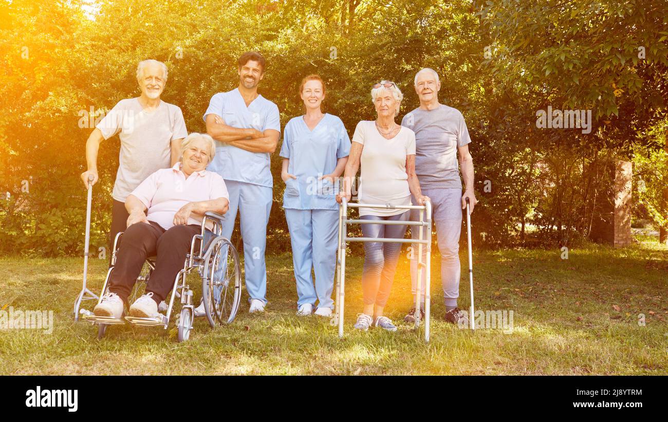 Gruppe von Senioren mit Menschen im Rollstuhl und mit Spaziergängern zusammen mit männlichen Krankenschwestern im Garten Stockfoto