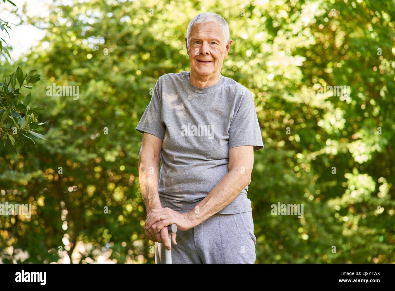 Alter Mann mit einem Gehstock nach einem Schlaganfall lernen, in der Rehabilitationsklinik im Garten zu gehen Stockfoto