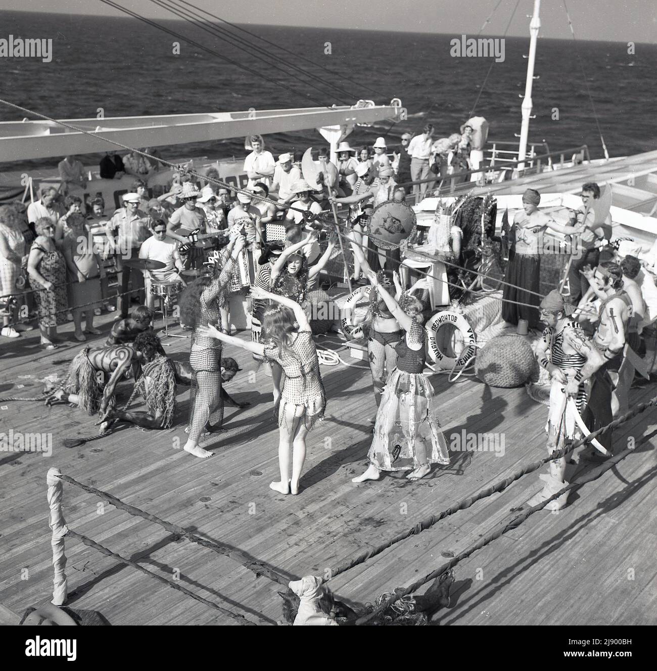 1960s, historisch, mitten im Ozean, an Deck des Sagafjord-Kreuzfahrtschiffs, spielt eine Band Musik als Passagiere, die sich verkleidet haben, um die Linienübergangszeremonie, eine Wassertaufe oder ein Ritual zu feiern, wenn ein Schiff den Äquator überquert, Wird manchmal als eine Intiation in den Hof von König Neptun bezeichnet. Stockfoto
