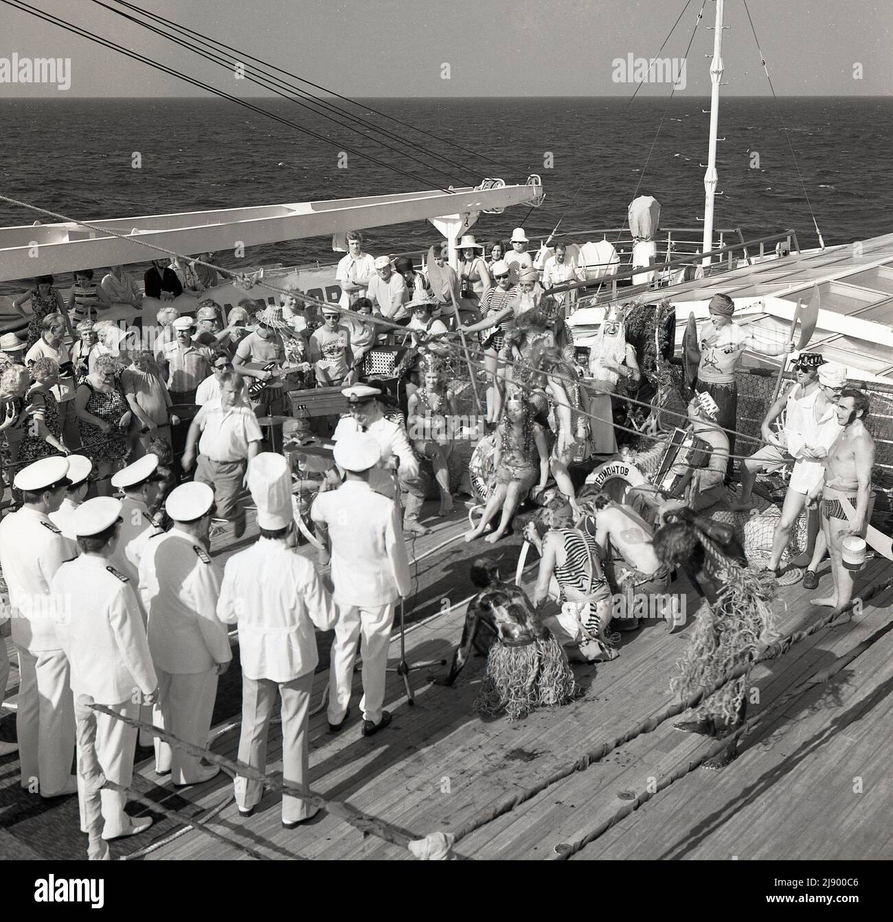 1960s, historisch, mitten im Ozean, an Deck des Sagafjord-Kreuzfahrtschiffs, spielt eine Band Musik als Passagiere, die sich verkleidet haben, um die Linienübergangszeremonie, eine Wassertaufe oder ein Ritual zu feiern, wenn ein Schiff den Äquator überquert, Wird manchmal als eine Intiation in den Hof von König Neptun bezeichnet. Stockfoto 1960s, historisch, mitten im Ozean, an Deck des Sagafjord-Kreuzfahrtschiffs, spielt eine Band Musik als Passagiere, die sich verkleidet haben, um die Linienübergangszeremonie, eine Wassertaufe oder ein Ritual zu feiern, wenn ein Schiff den Äquator überquert, Wird manchmal als eine Intiation in den Hof von König Neptun bezeichnet. Stockfoto