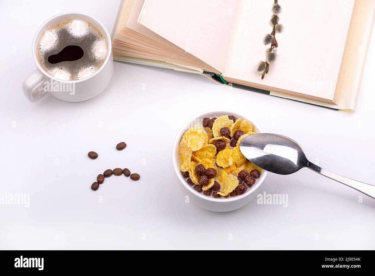 Schon das Frühstück war traurig. Müsli mit Milch, Kaffee, ein Buch und ein trauriges Lächeln aus Kaffeebohnen. Modell Stockfoto