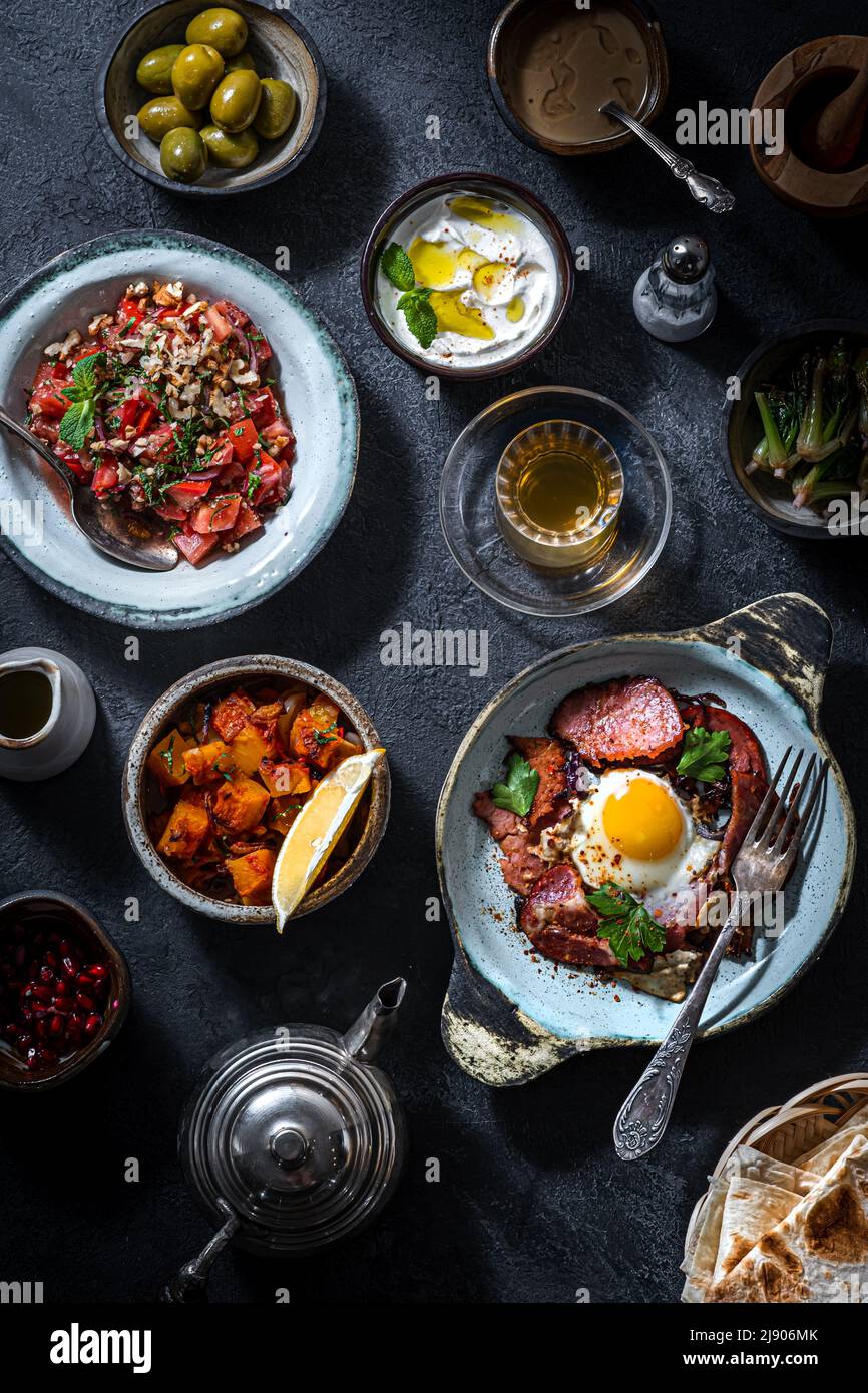 Türkischer Frühstückstisch. Flachgebäck, Gemüse, Gemüse, Gemüse, Oliven, Käse, Spiegeleier, Gewürze, Marmeladen, Honig, Tee in Kupferköpfen und Tulpengläsern Stockfoto