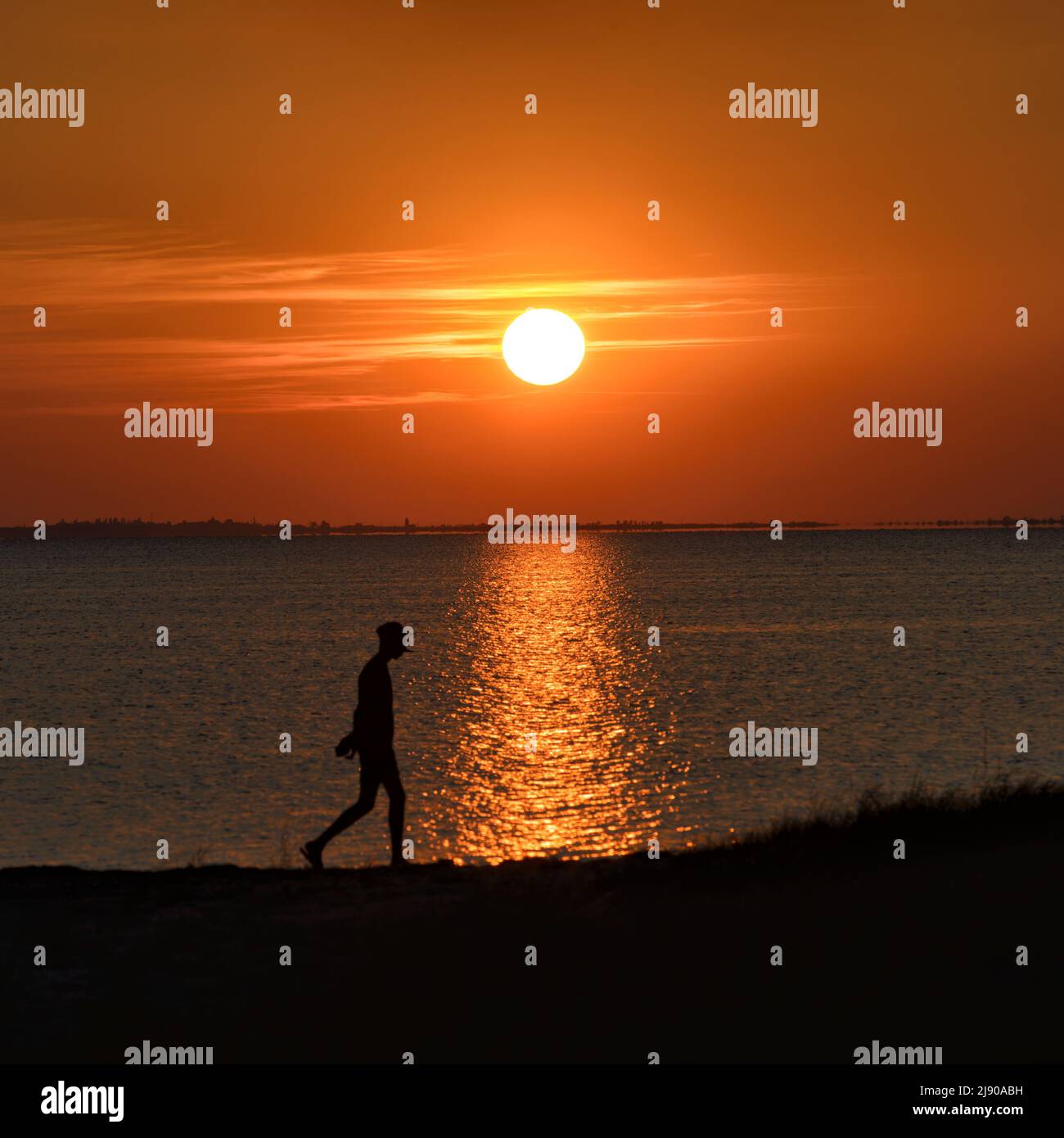 Dramatischer Sonnenuntergang am Meer mit der Silhouette einer wandelenden Person im Rahmen im Licht der untergehenden Sonne. Asowschen Meer, Ukraine Stockfoto