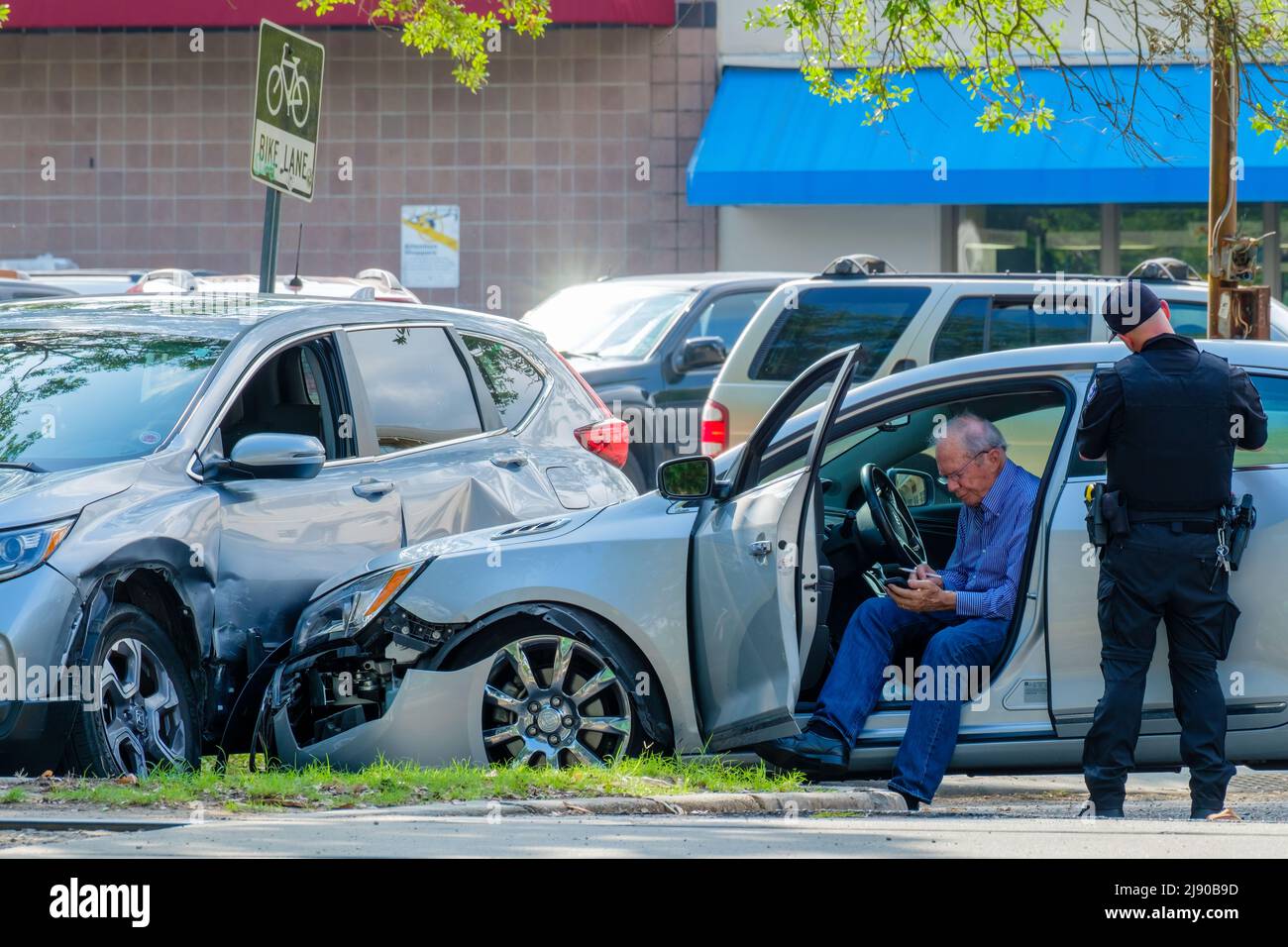 NEW ORLEANS, LA, USA - 9. MAI 2022: Autounfall-Szene mit beschädigten Autos, Polizist beim Schreiben einer Fahrkarte und Fahrer (Telefonwahl) Stockfoto