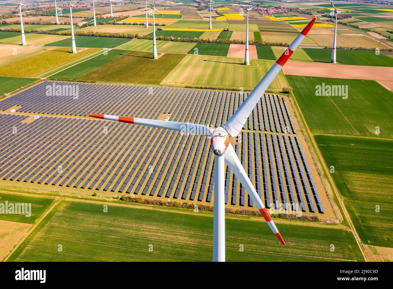 Riesige Windturbinen zwischen landwirtschaftlichem Land und einem Solarpark in einem ländlichen Gebiet aus Drohnenperspektive, Deutschland Stockfoto