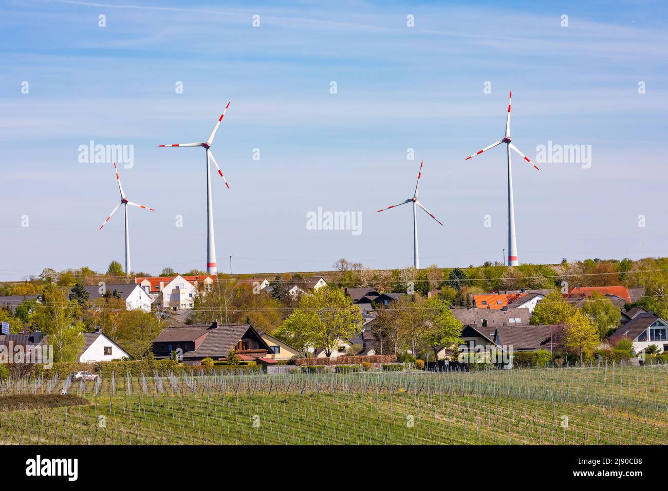 Eine Siedlung in einer ländlichen Landschaft mit Feldern und Reben wird von riesigen Windkraftanlagen dominiert Stockfoto