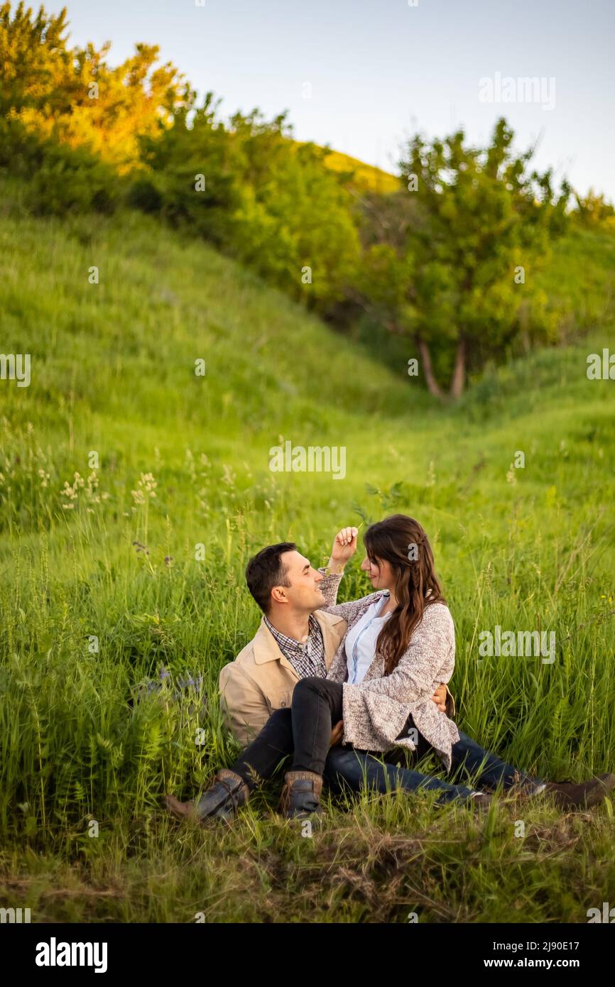 Liebevolles Hipster-Paar, das auf dem Feld läuft, küsst und die Hände hält, umarmt, im Sommer bei Sonnenuntergang im Gras liegt. valentinstag. Stockfoto