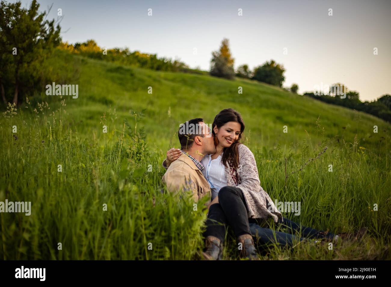 Liebevolles Hipster-Paar, das auf dem Feld läuft, küsst und die Hände hält, umarmt, im Sommer bei Sonnenuntergang im Gras liegt. valentinstag. Stockfoto