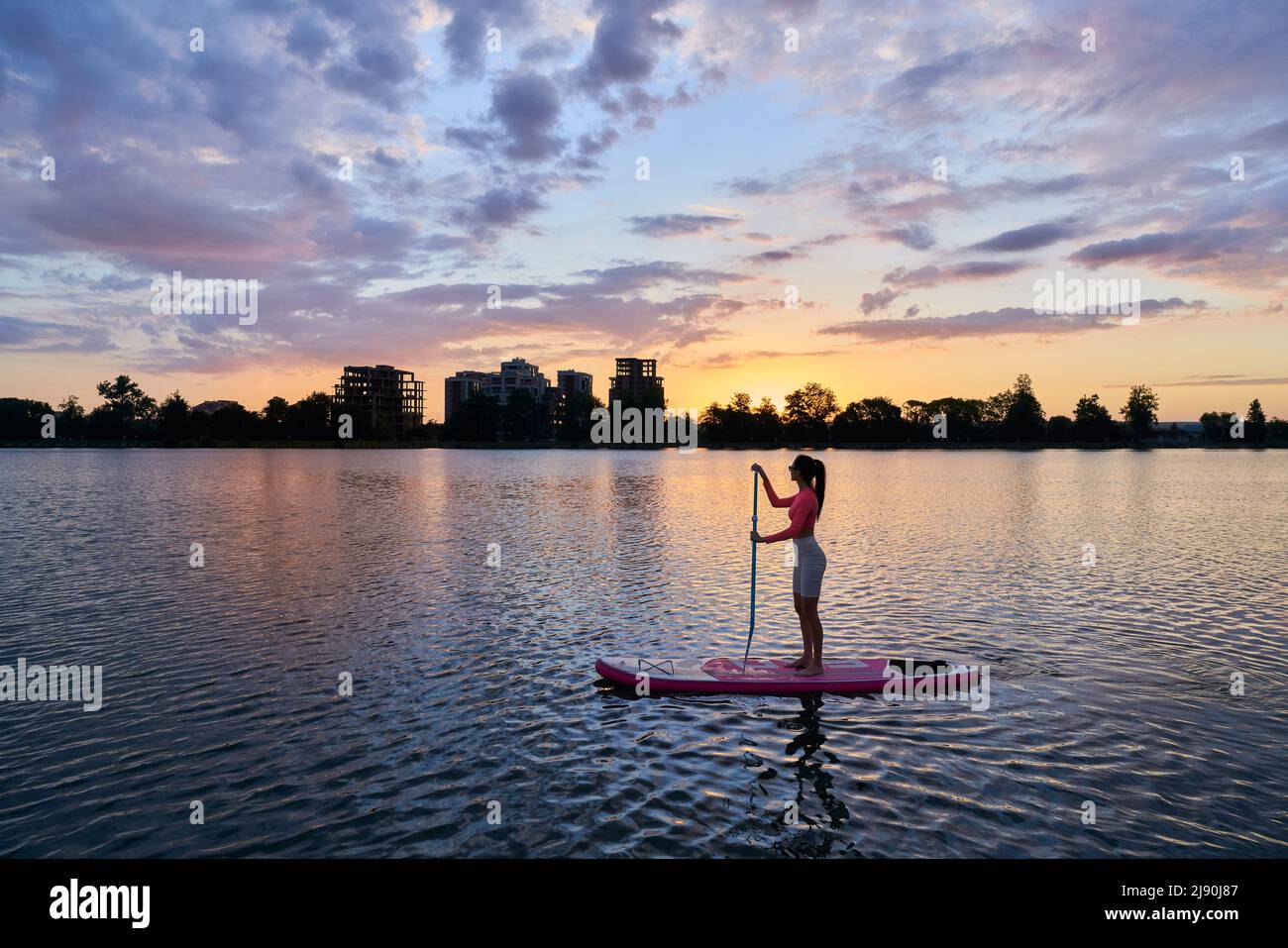 Kaukasische Frau mit schlankem Körpertraining auf dem Brett während des Sonnenuntergangs im Sommer. Junge Brünette genießen Abendzeit während der Wasseraktivität. Stockfoto