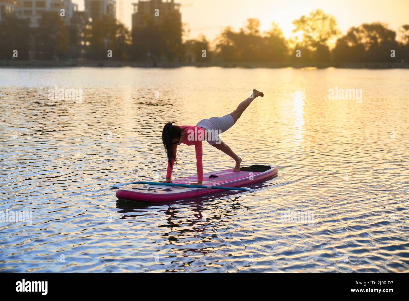 Gesunde und fit Frau balanciert auf supboard während Yoga-Übungen. Kaukasische Brünette in Sportbekleidung mit aktiven Training auf Sommersee. Stockfoto