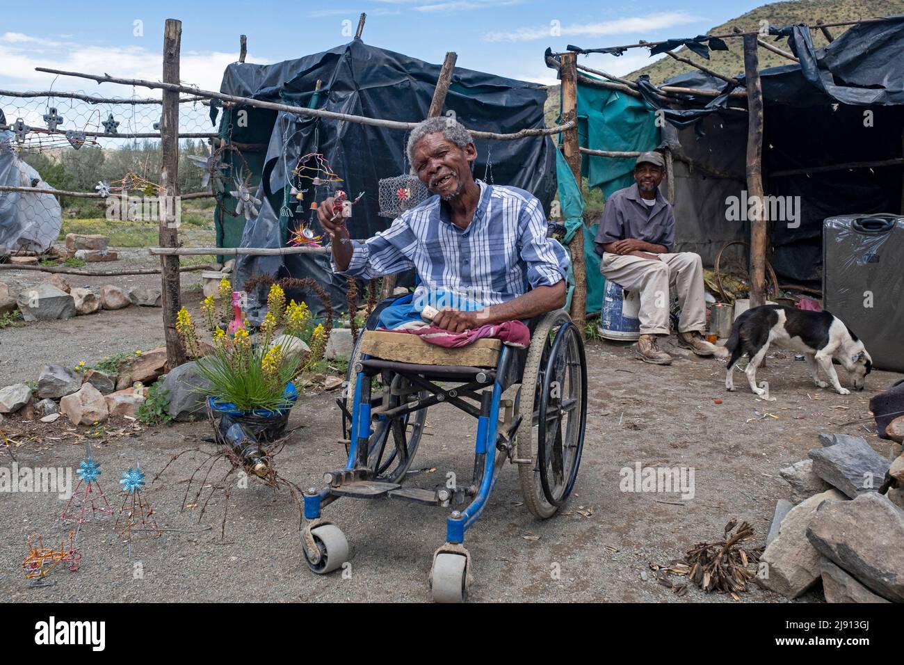 Behinderter schwarzer Mann im Rollstuhl, der im Dorf Nieu-Bethesda / New Bethesda, Ostkap, Südafrika, Souvenirs aus Schrott verkauft Stockfoto
