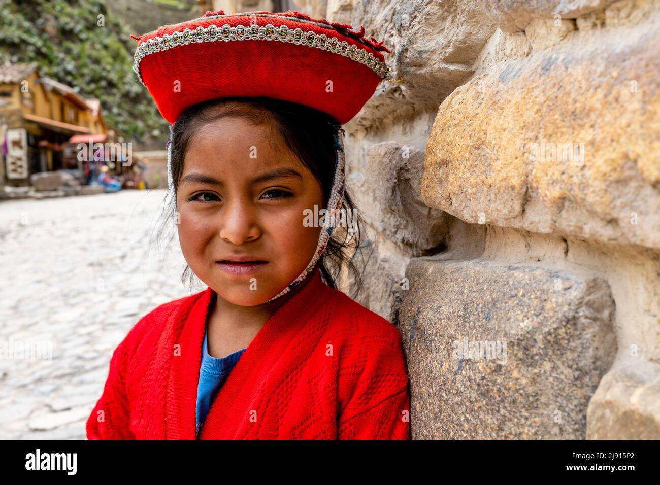 Ein Indigenes Mädchen In Traditioneller Tracht Vor Der Archäologischen Stätte Ollantaytambo, Ollantaytambo, Dem Heiligen Tal, Cusco Region, Peru. Stockfoto