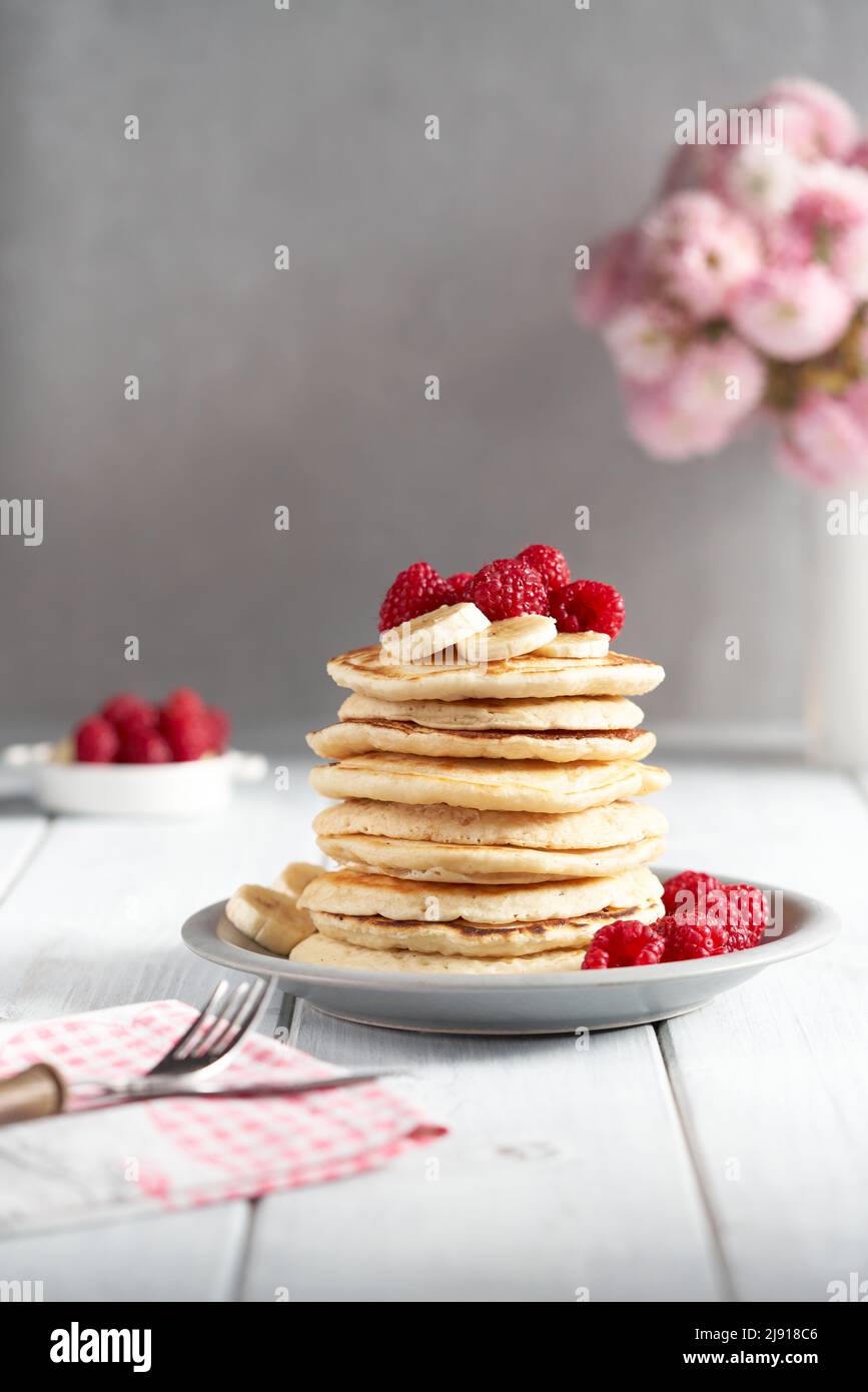 Amerikanische Pfannkuchen mit Himbeeren und Bananen auf hellem, minimalem Hintergrund. Leckere Pfannkuchen auf Holztisch mit Früchten. Stockfoto