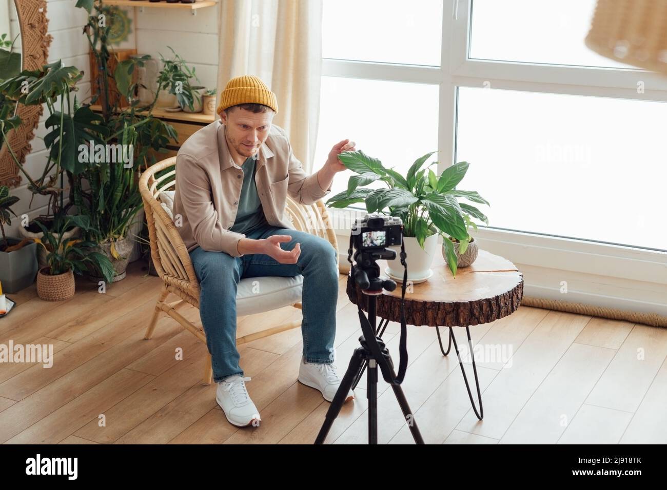 Blogger mittleren Alters mit Videoaufnahme in gemütlicher Inneneinrichtung im Boho-Stil. Mann, der zu Hause Videos aufzeichnet Stockfoto