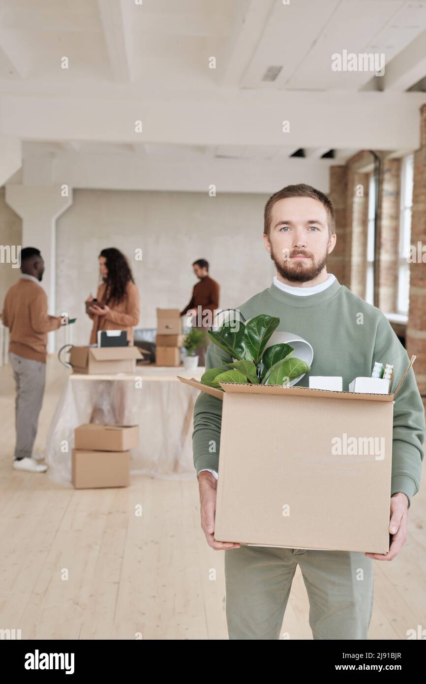 Porträt eines seriöse bärtigen Managers, der einen Karton voller persönlicher Sachen hält, während er in ein neues Büro umzieht Stockfoto