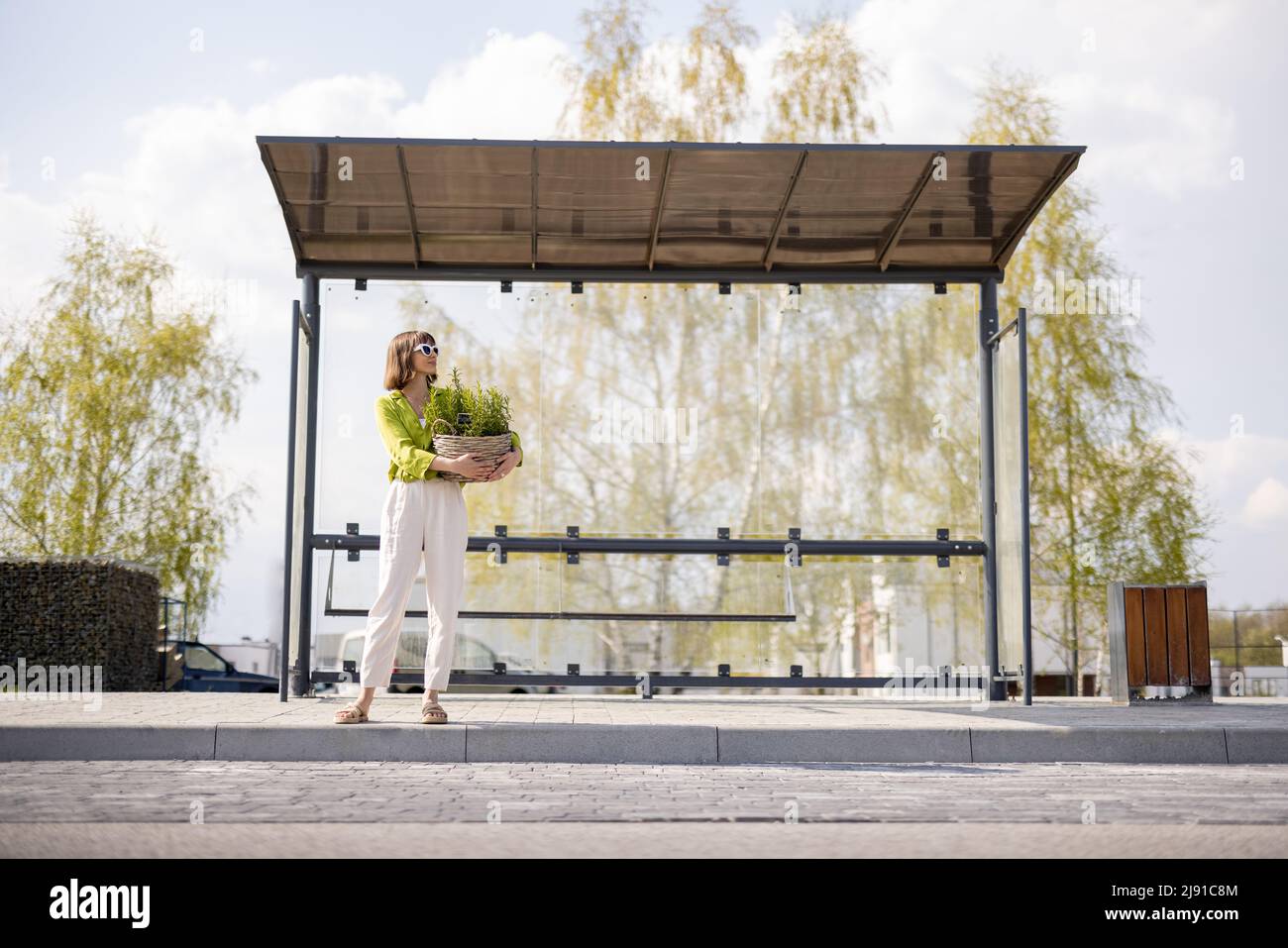 Frau mit Blumentopf an der modernen Bushaltestelle Stockfoto