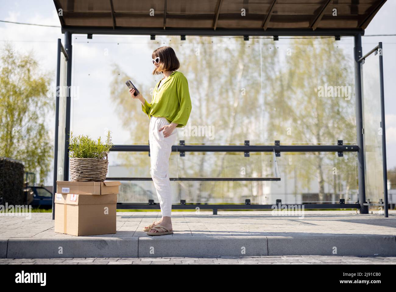 Frau mit Paketen und Blumentopf an einer Bushaltestelle Stockfoto