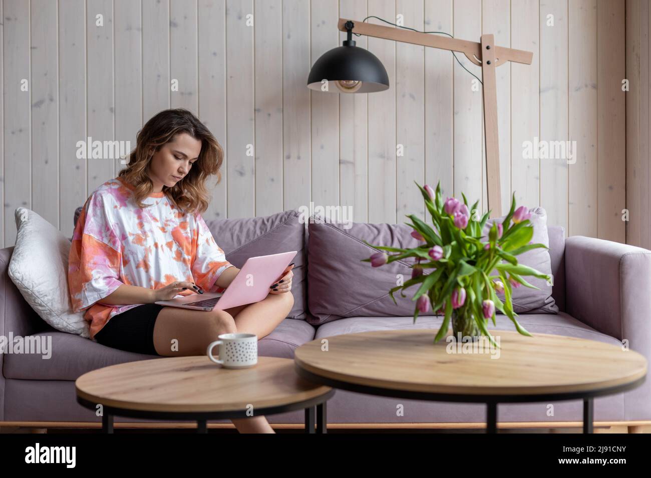 Online zu Hause arbeiten. Junge charmante braunhaarige Frau mit langen Haaren in bequemer Heimkleidung arbeitet zu Hause im Internet auf einem gemütlichen Sofa sitzend Stockfoto