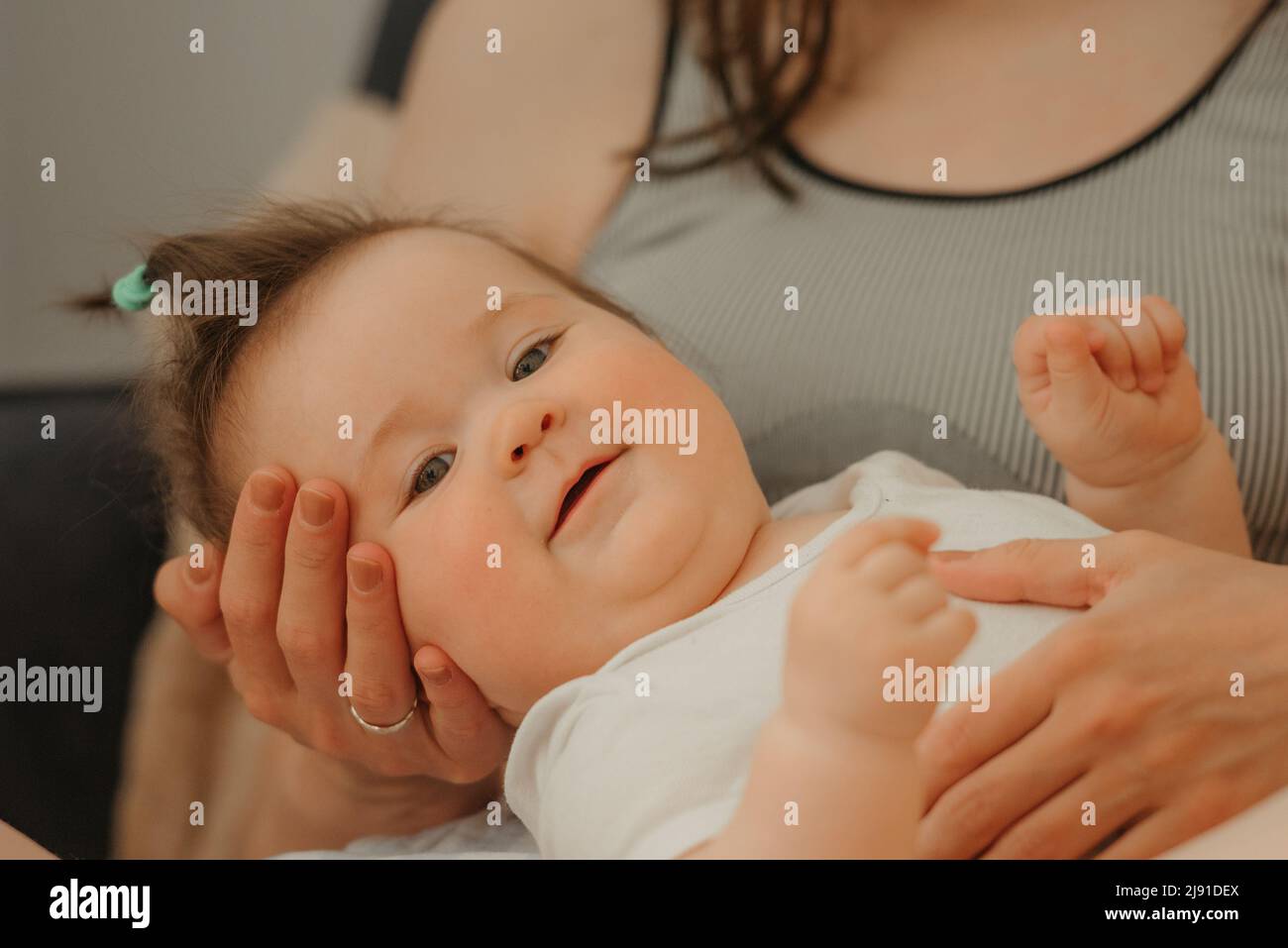 Ein Porträt eines 7 Monate dauernden Mädchens in den Armen ihrer Mutter, die lächelt Stockfoto