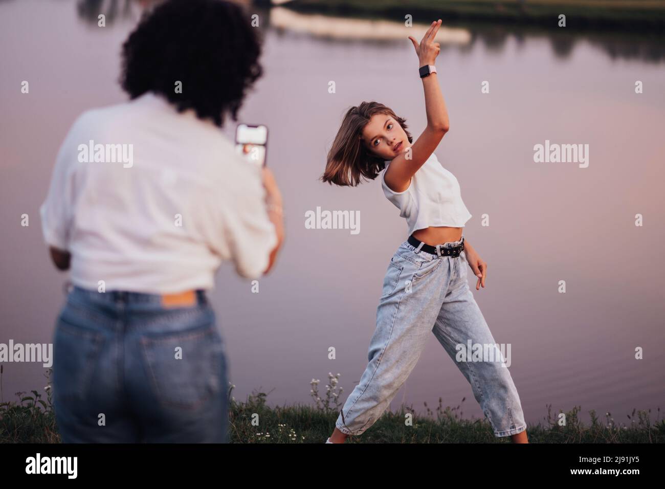 Mutter nimmt Foto ihrer Teenage-Tochter auf dem Smartphone für Social Network Outdoors by the Lake auf Stockfoto