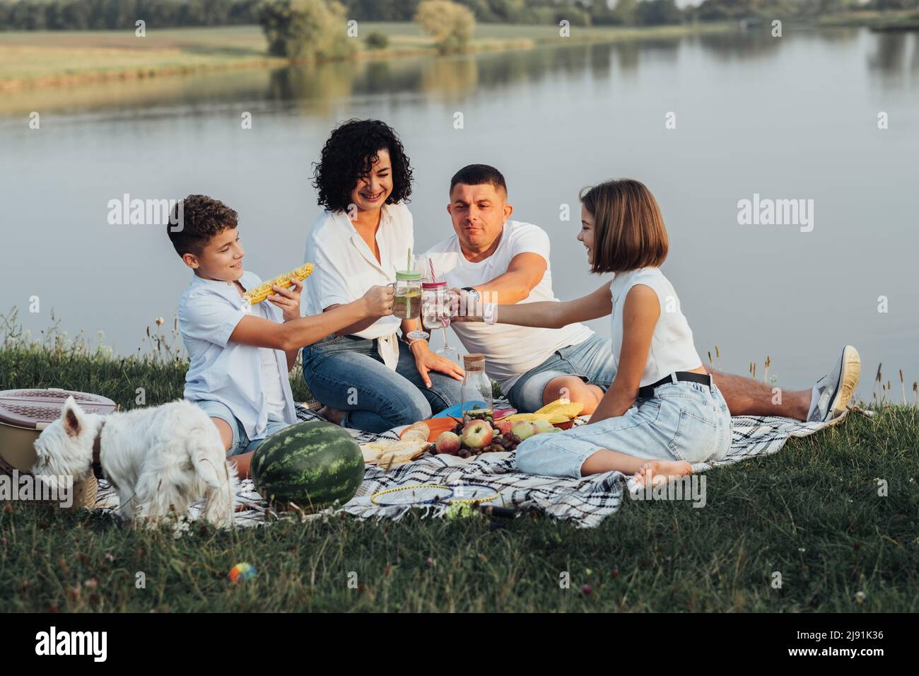 Glückliche vier Mitglieder Familie mit Hund beim Picknick bei Sonnenuntergang, fröhliche Mutter und Vater mit zwei Teenagern Kinder und Haustier genießen Wochenende im Freien Stockfoto
