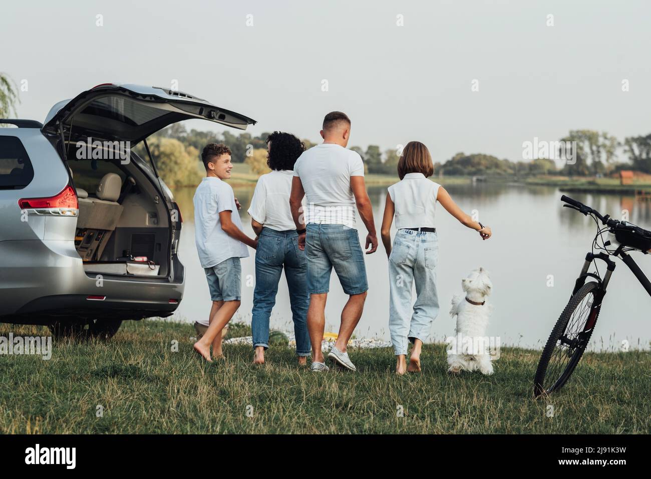 Vier Mitglieder Familie mit dem Minivan-Auto unterwegs und Picknick bei Sonnenuntergang am See, Mutter und Vater mit zwei Teenagekindern und Pet West Stockfoto