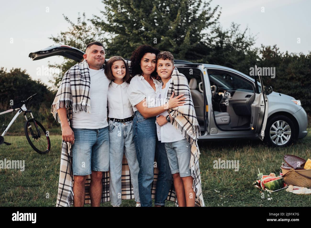 Vier Mitglieder Familie beim Picknick bei Sonnenuntergang, eine Mutter und ein Vater mit zwei Teenagerkindern genießen einen Wochenendausflug mit dem Auto Stockfoto