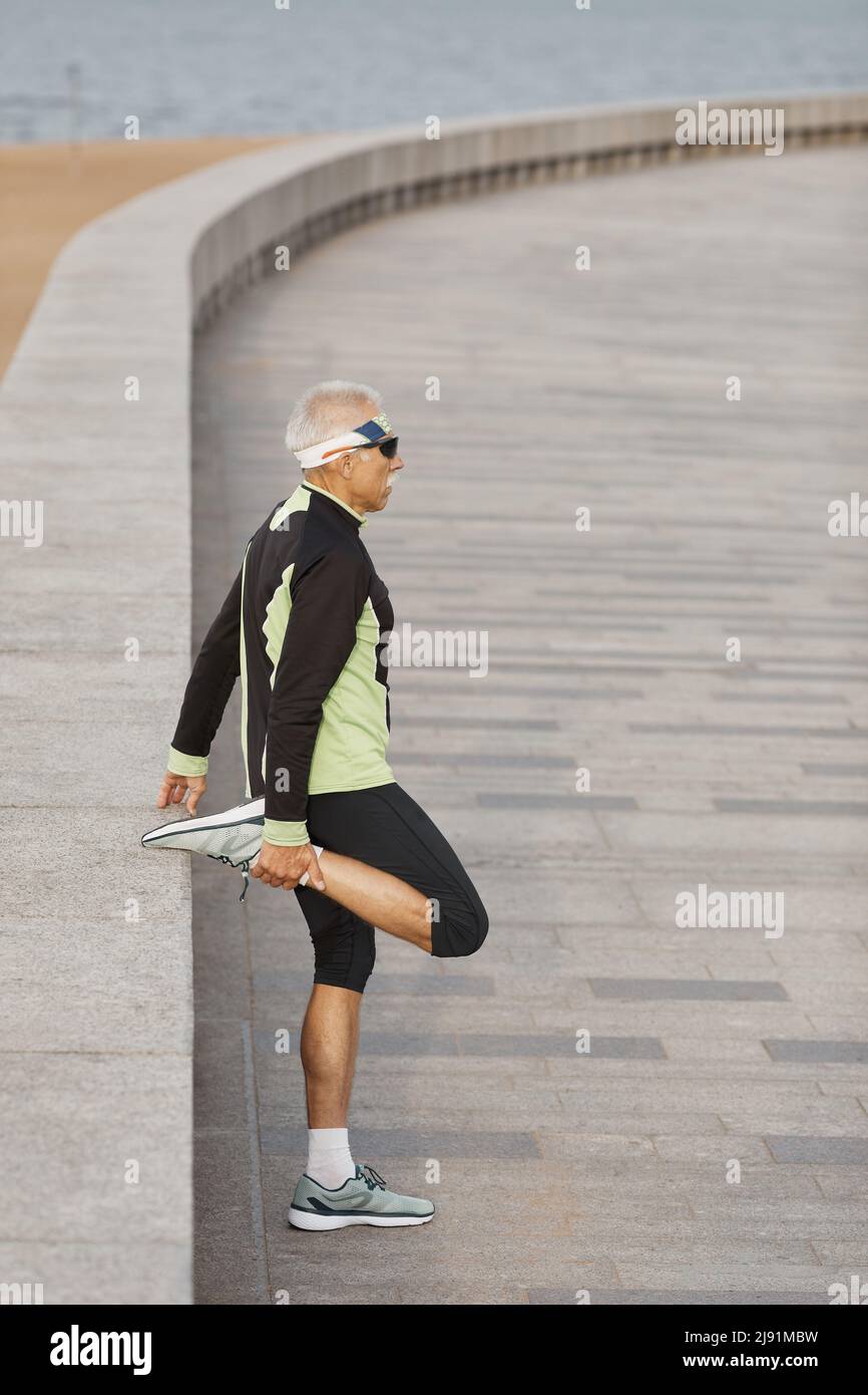 Vertikale Seitenansicht Schuß von gealterten Mann sportliches Outfit tun leg stretching Übung morgens Stockfoto