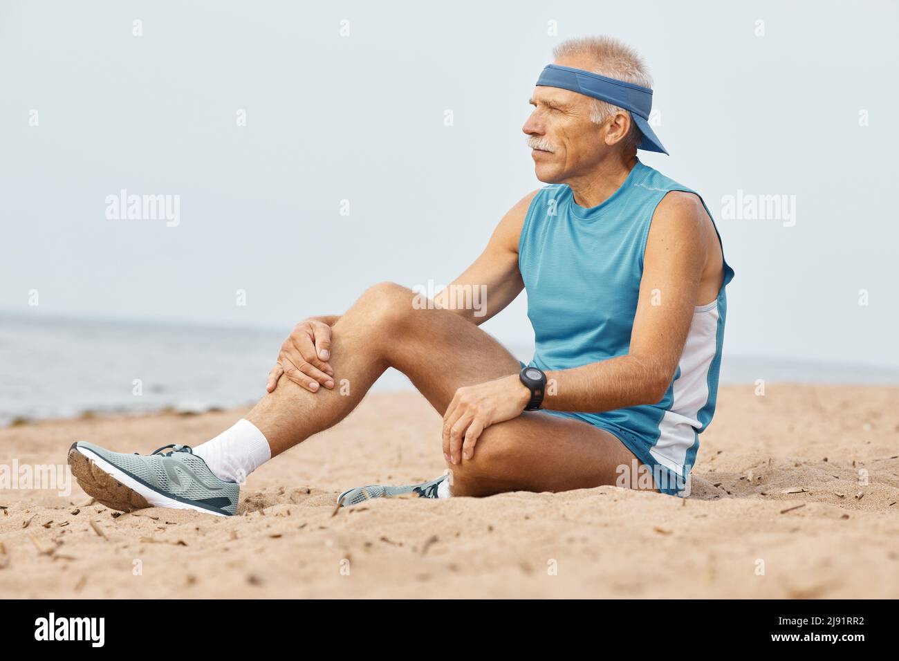 Horizontale Schuß von gealterten Mann sportliches Outfit sitzen auf Sand suchen Stockfoto