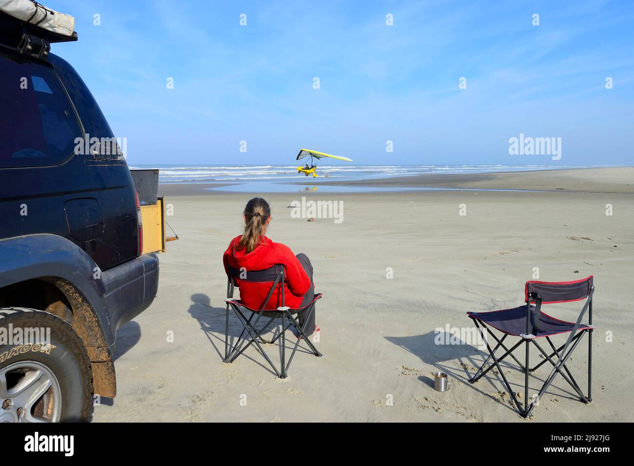 Frau, die auf einem Campingstuhl neben einem Geländewagen am Strand sitzt und ein leichtes Flugzeug beim Start beobachtet, Ulm, Torres, Rio Grande do Sul, Brasilien Stockfoto