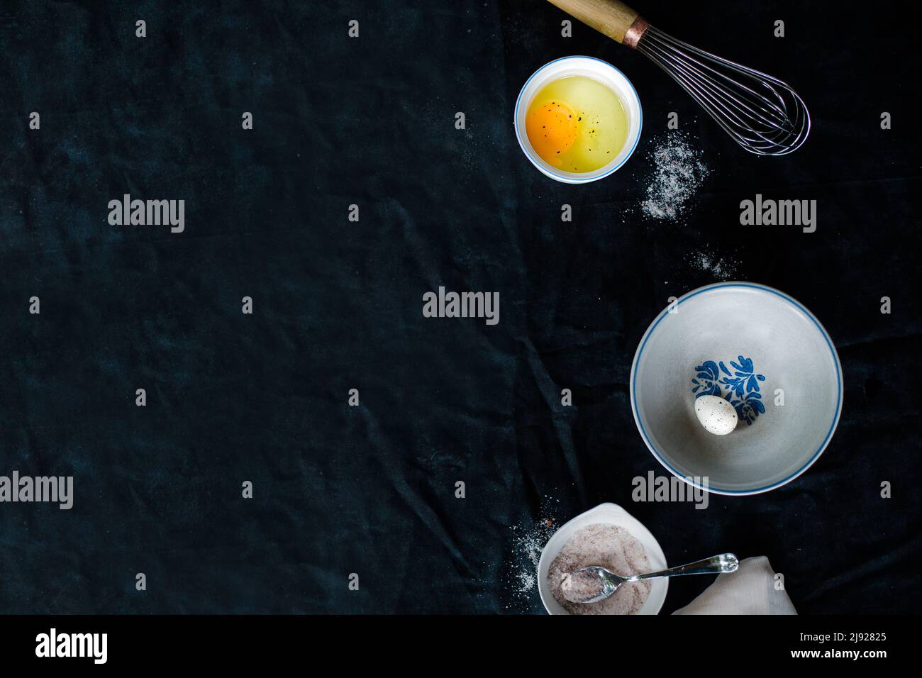 Eier und Eierschalen auf dunklem Hintergrund, umgeben von Schüsseln und einem Schneebesen Stockfoto