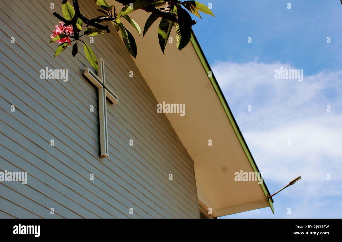 Das Kreuz auf der Mauer der Vereinten Kirche Bethel III. Im Dorf Keapara, Zentralprovinz, PNG, mit tropischen Frangipani-Blüten vor einem blauen Himmel Stockfoto
