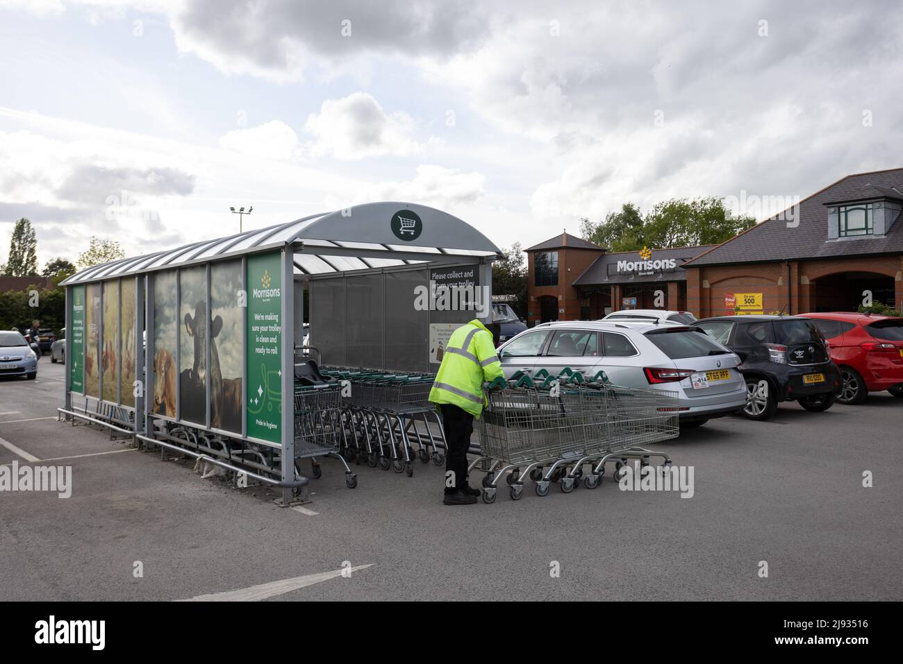 Mann in gelber reflektierender Weste bewegt Einkaufswagen am Morrisons Supermarkt Starbeck Store Parkplatz Stockfoto