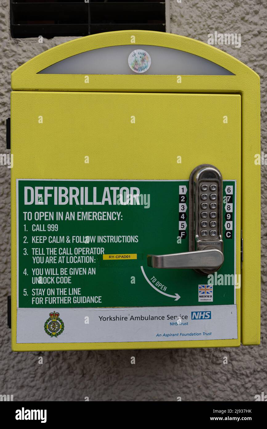 Nahaufnahme eines gelben Defibrillatorkastens an einer Wand in Knaresborough Yorkshire, Großbritannien Stockfoto