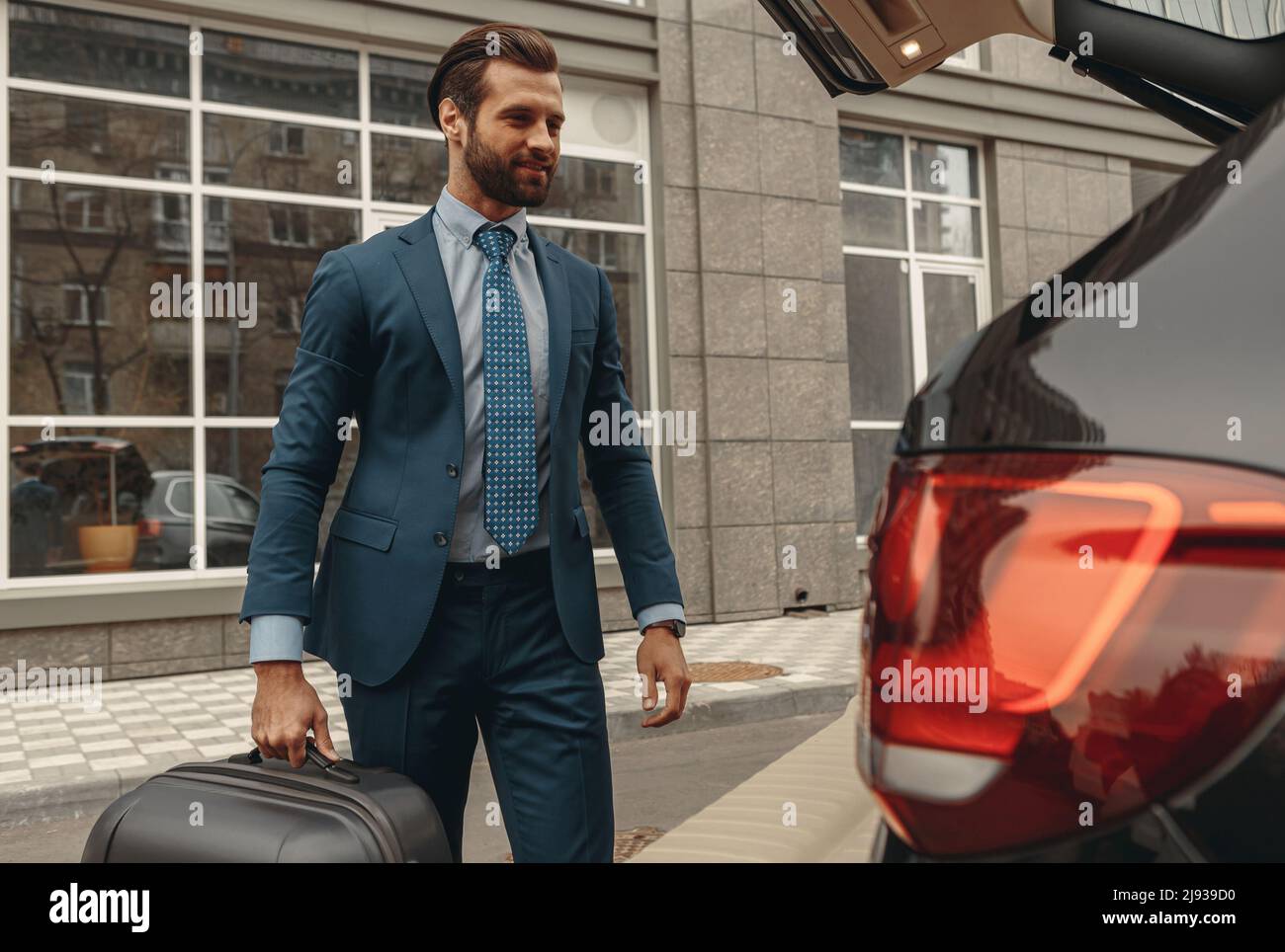 Glücklicher bärtiger Mann in formeller Kleidung geht auf eine Reise durch ein Auto Stockfoto