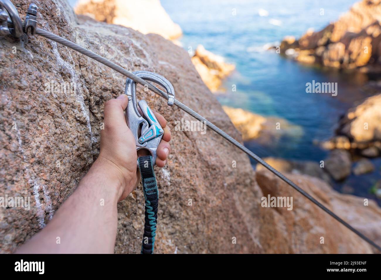 Klettergriffe Details die Hand des jungen Mannes auf Felsen über dem Meer mit Seil und Helm. Stockfoto