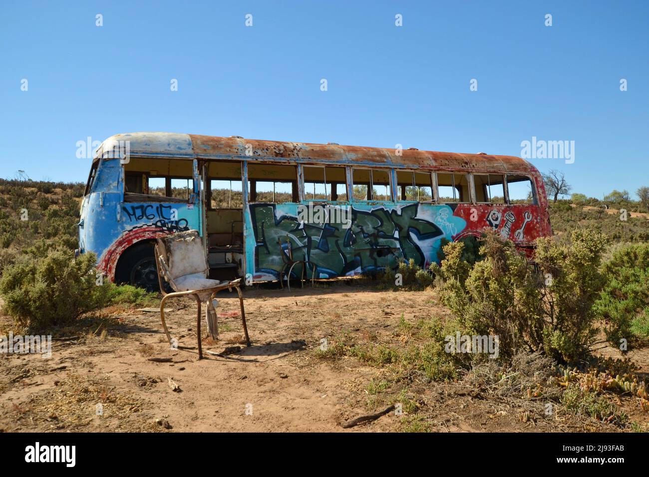 Ein alter Oldtimer-Bus im Outback Australiens, mit Graffiti und Tags bedeckt, ohne Fenster oder Motor und davor ein alter Küchenstuhl. Stockfoto