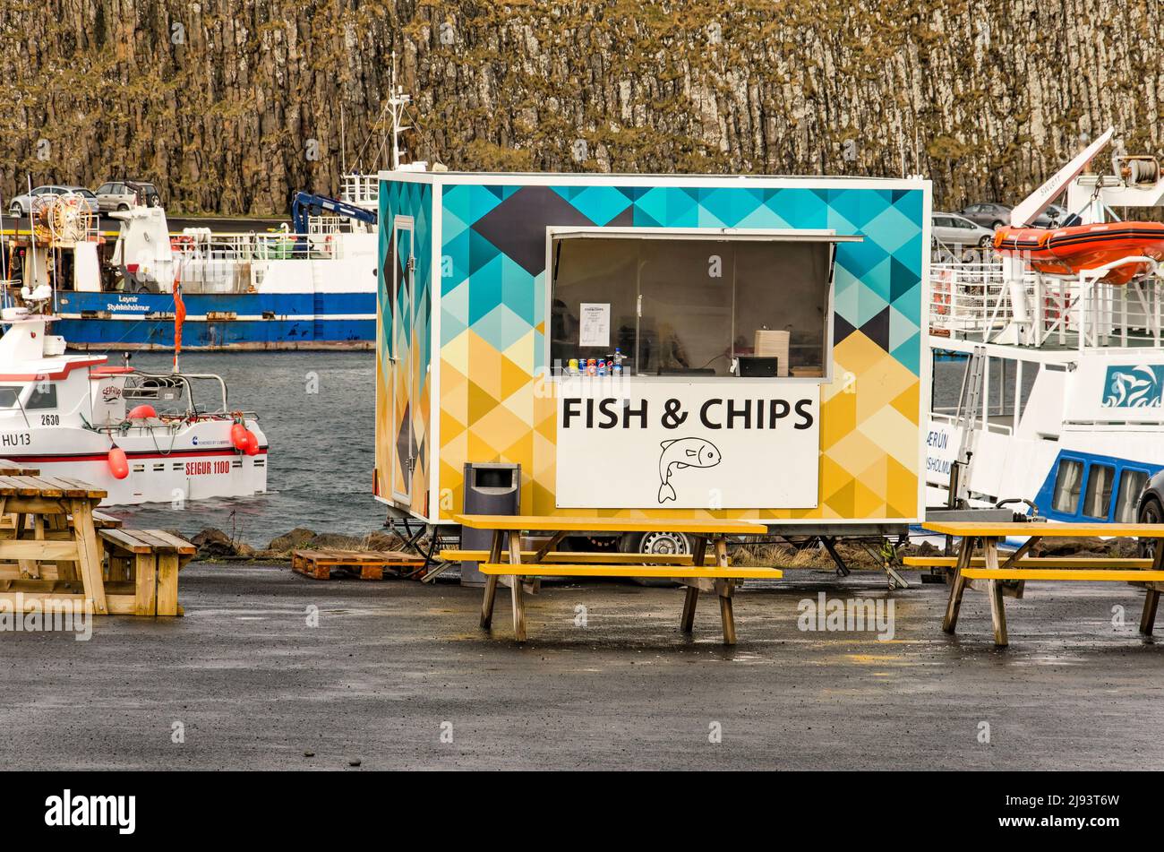 Stykkisholmur, Island, 3. Mai 2022: Bunte Fische und Chips stehen am Kai im Stadthafen mit verschiedenen Booten und einer Felswand im Backgr Stockfoto